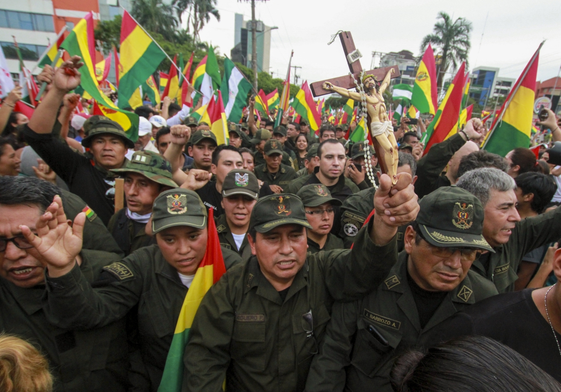 A police officer holds a crucifix among comrades and people taking to the streets of Santa Cruz to celebrate the resignation of Bolivian President Evo Morales on November 10, 2019. - Morales announced his resignation on Sunday, caving in following three weeks of sometimes-violent protests over his disputed re-election after the army and police withdrew their backing. (Photo by DANIEL WALKER / AFP)