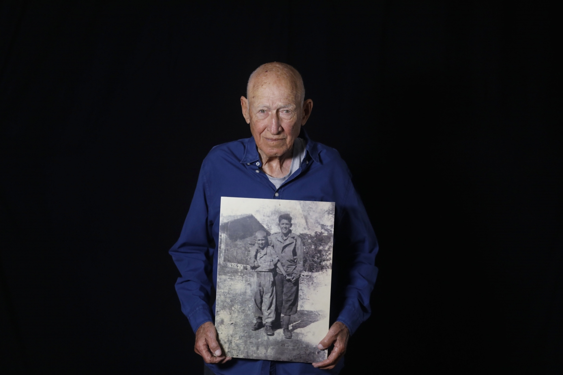 Danny Chanoch posa com uma foto dele e de seu irmão mais velho Uri após a guerra(Foto: MENAHEM KAHANA/AFP)