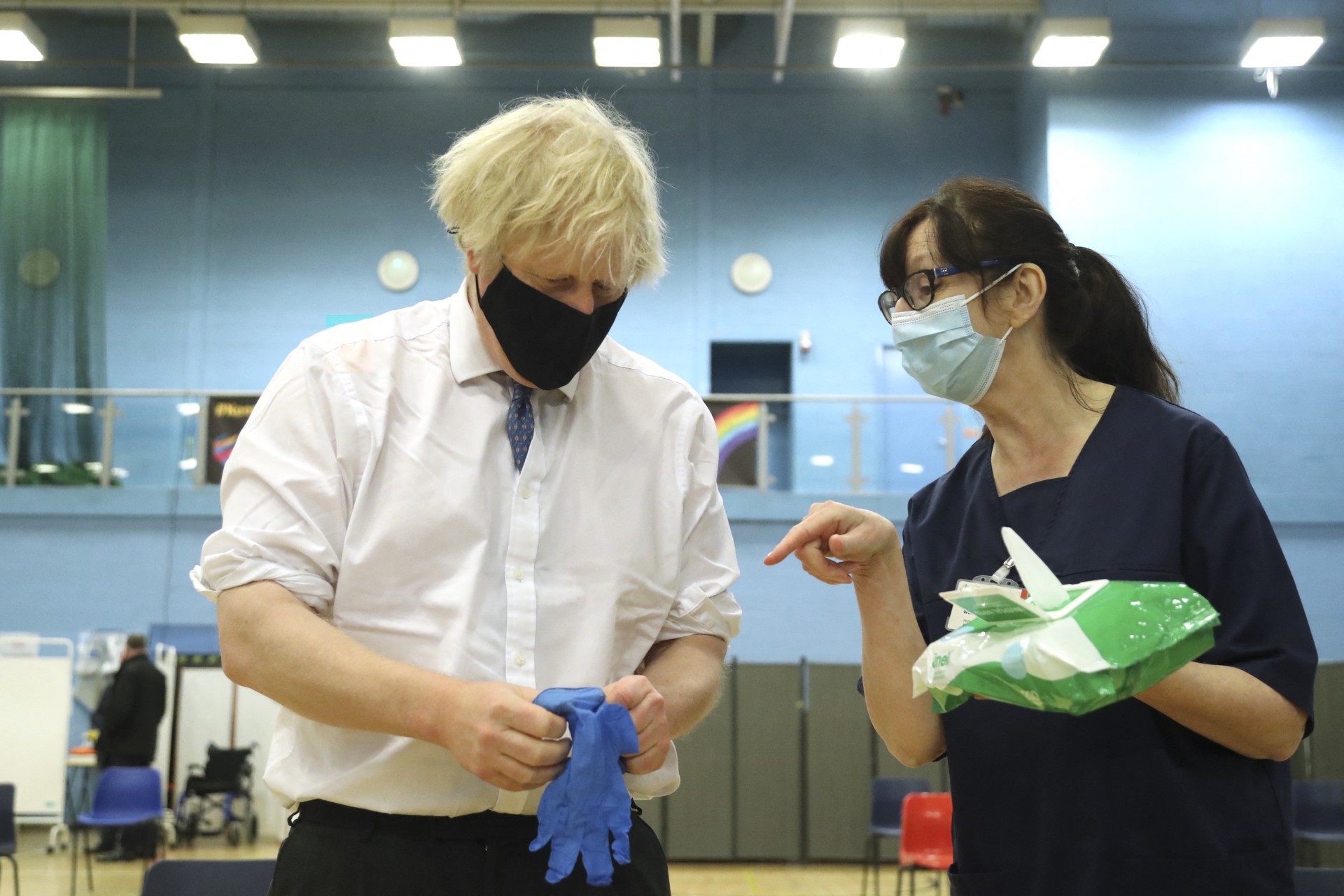 O primeiro-ministro britânico Boris Johnson fala com o trabalhadora de saúde Wendy Warren enquanto ele calça um par de luvas médicas durante visita a um centro de vacinação no Cwmbran Stadium, sul do País de Gales em 17 de fevereiro de 2021. (Foto de Geoff Caddick / vários fontes / AFP) (Foto: AFP)