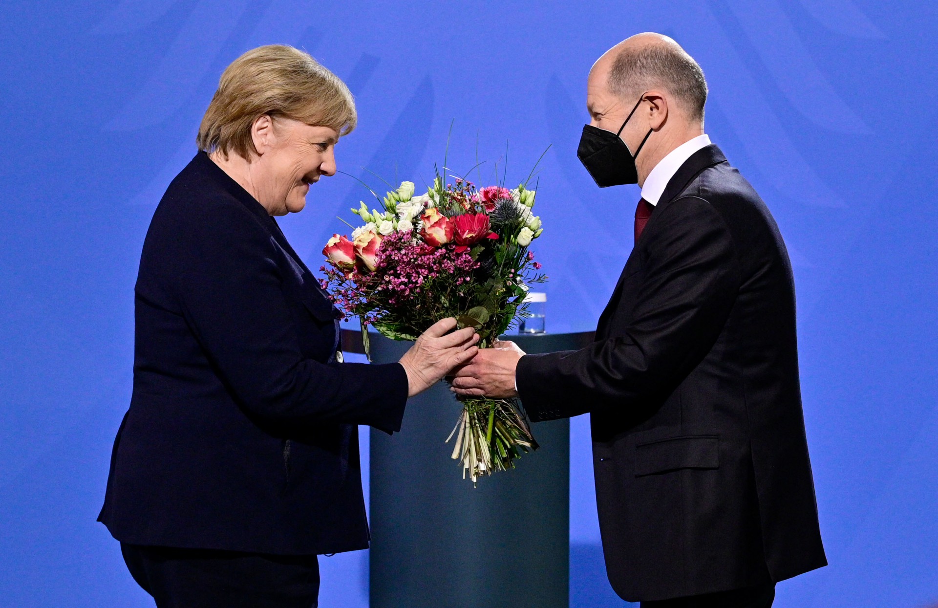 O chanceler alemão Olaf Scholz dá um buquê de flores para sua antecessora Angela Merkel depois que ela lhe entregou o cargo na Chancelaria em Berlim em 8 de dezembro de 2021(Foto: John MACDOUGALL / AFP)