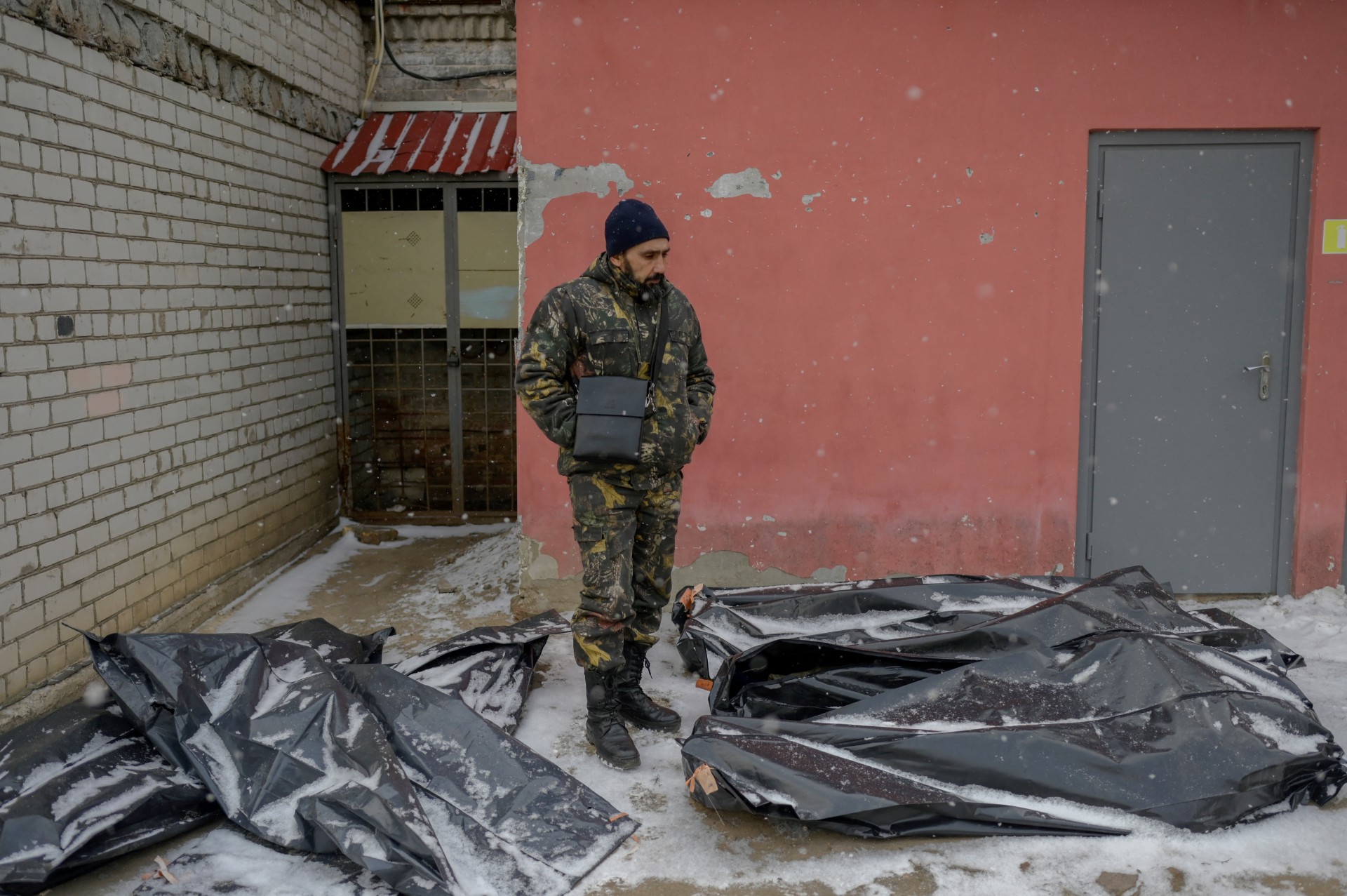 UM UCRANIANO camuflado ao lado de sacos de corpos cobertos de neve no quintal de um necrotério em Mykolaiv, uma cidade às margens do Mar Negro que está sob ataque russo  (Foto: BULENT KILIC / AFP)