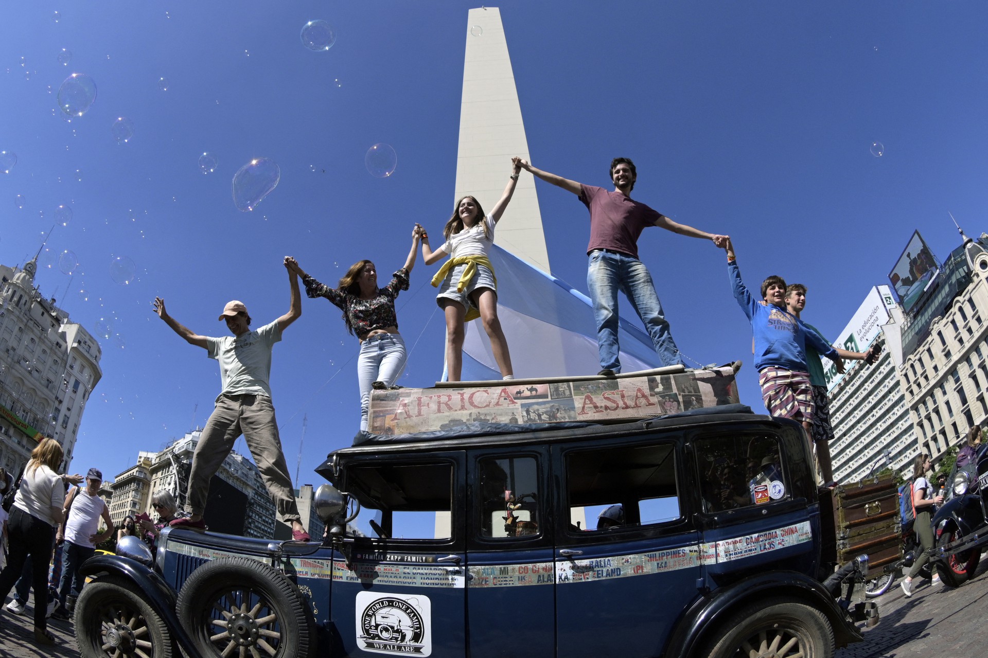 A família argentina Zapp acena em cima de seu carro, um Graham-Paige 1928, na praça Republica, em Buenos Aires, em 13 de março de 2022, depois de terminar uma viagem de 22 anos pelo mundo que começou em 23 de janeiro de 2000. (Foto: JUAN MABROMATA / AFP)