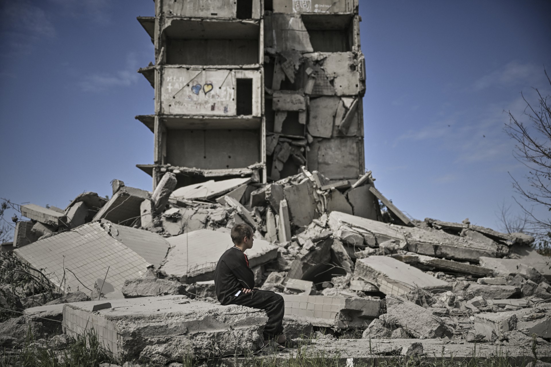 Um menino sentado em frente a um prédio danificado após um ataque em Kramatorsk, na região leste ucraniana de Donbas, em 25 de maio de 2022 (Foto: ARIS MESSINIS / AFP)