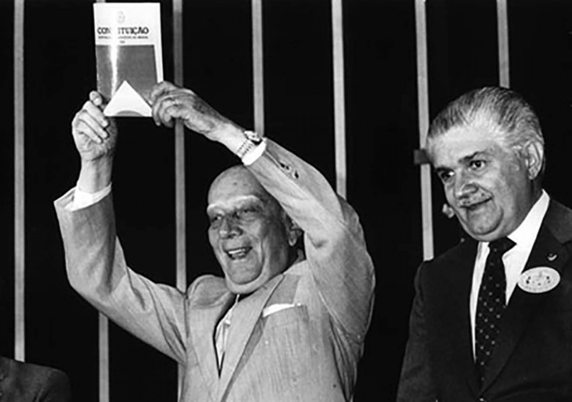 Ulysses Guimarães, presidente da Assembleia Constituinte, exibe a nova Constituição. Ao seu lado, o político cearense Mauro Benevides. 5 de outubro de 1988 (Foto: Wikimedia Commons)