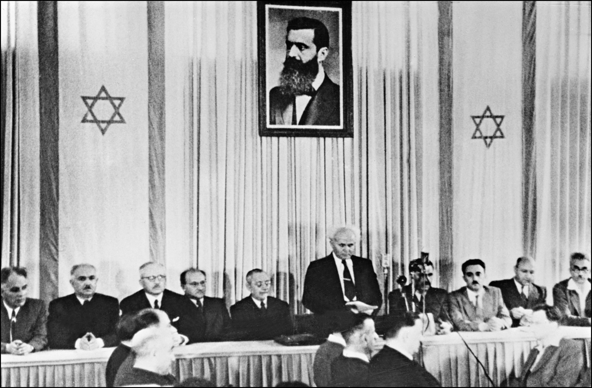 Nesta foto de arquivo tirada em 14 de maio de 1948, o primeiro-ministro israelense David Ben-Gurion (em pé sob um enorme retrato de Theodor Herzl, o fundador do sionismo político, cercado pelos membros do Conselho Nacional Judaico, proclama o estabelecimento do estado de Israel, em Tel Aviv(Foto: INTERCONTINENTALE / AFP)