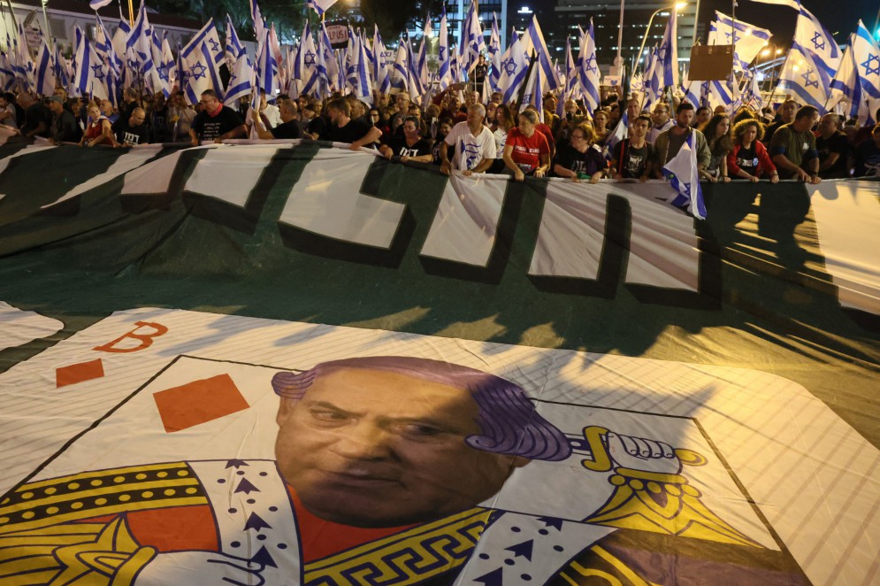 Manifestantes agitam uma faixa com o retrato do primeiro-ministro Benjamin Netanyahu enquanto se reúnem para protestar contra o projeto de reforma judicial do governo israelense, em Tel Aviv, em 6 de maio de 2023.(Foto: JACK GUEZ / AFP)