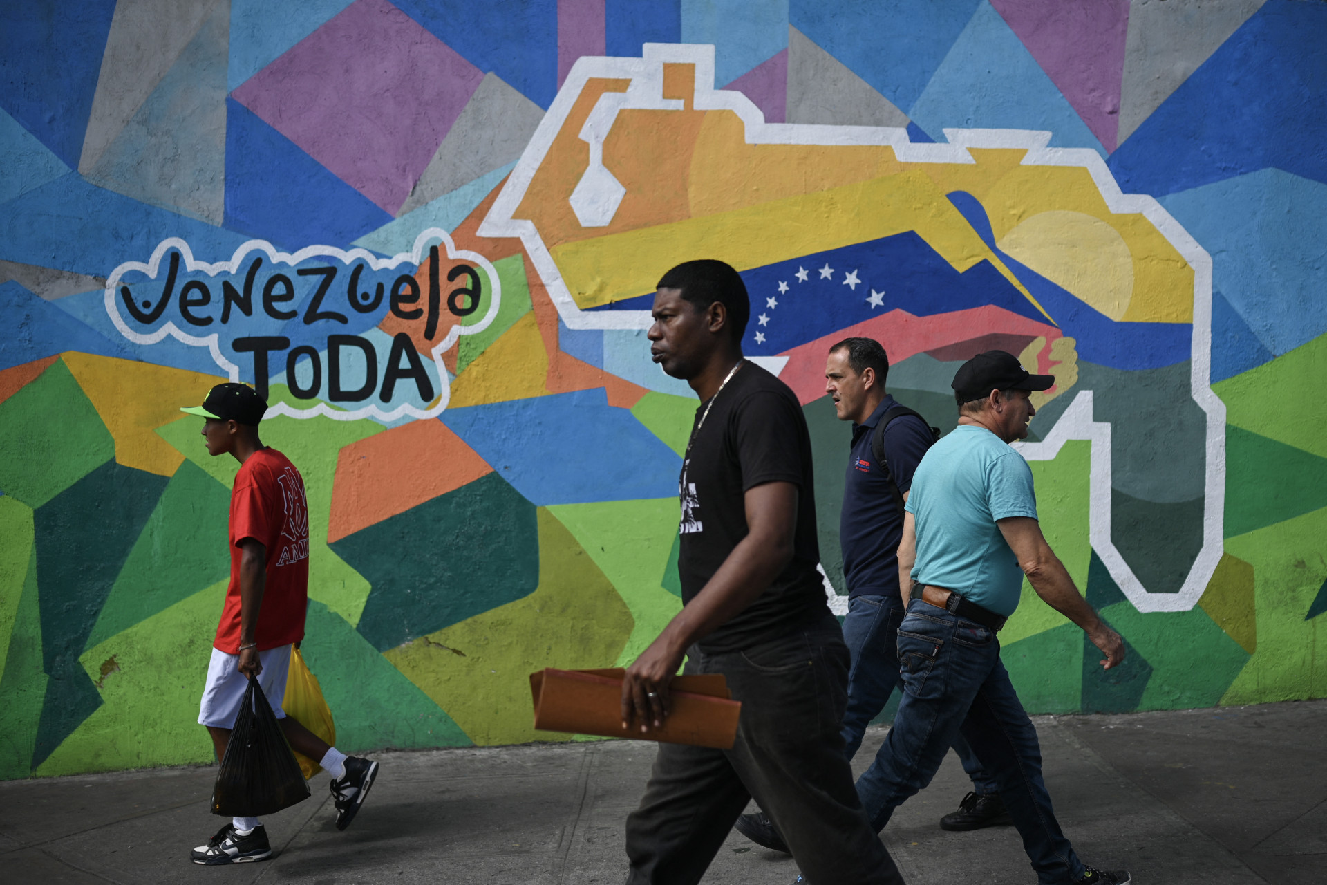 ￼Venezuelanos caminham diante de mural da campanha sobre o referendo sobre a anexação de território da Guiana (Foto: Federico PARRA / AFP)