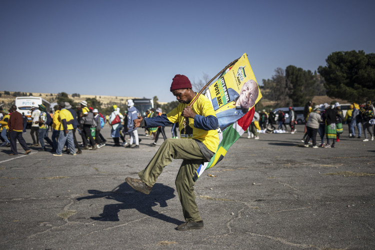 Um apoiador do Congresso Nacional Africano (ANC) dança enquanto agita uma imagem do ANC e do presidente sul-africano Cyril Ramaphosa, ao chegar para o último comício do ANC no Estádio FNB em Joanesburgo, em 25 de maio de 2024(Foto: MICHELE SPATARI / AFP)