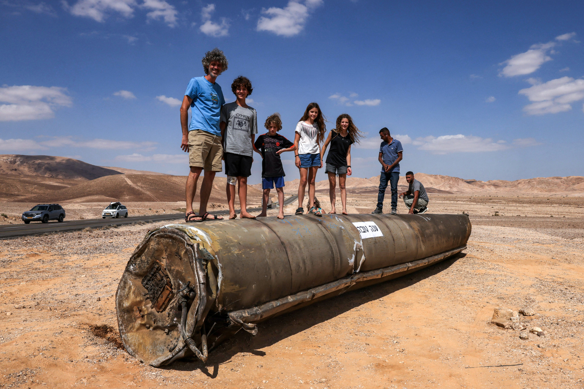 ￼PESSOAS em cima dos restos de um míssil iraniano no deserto de Neguev, em Israel (Foto: Menahem KAHANA / AFP)