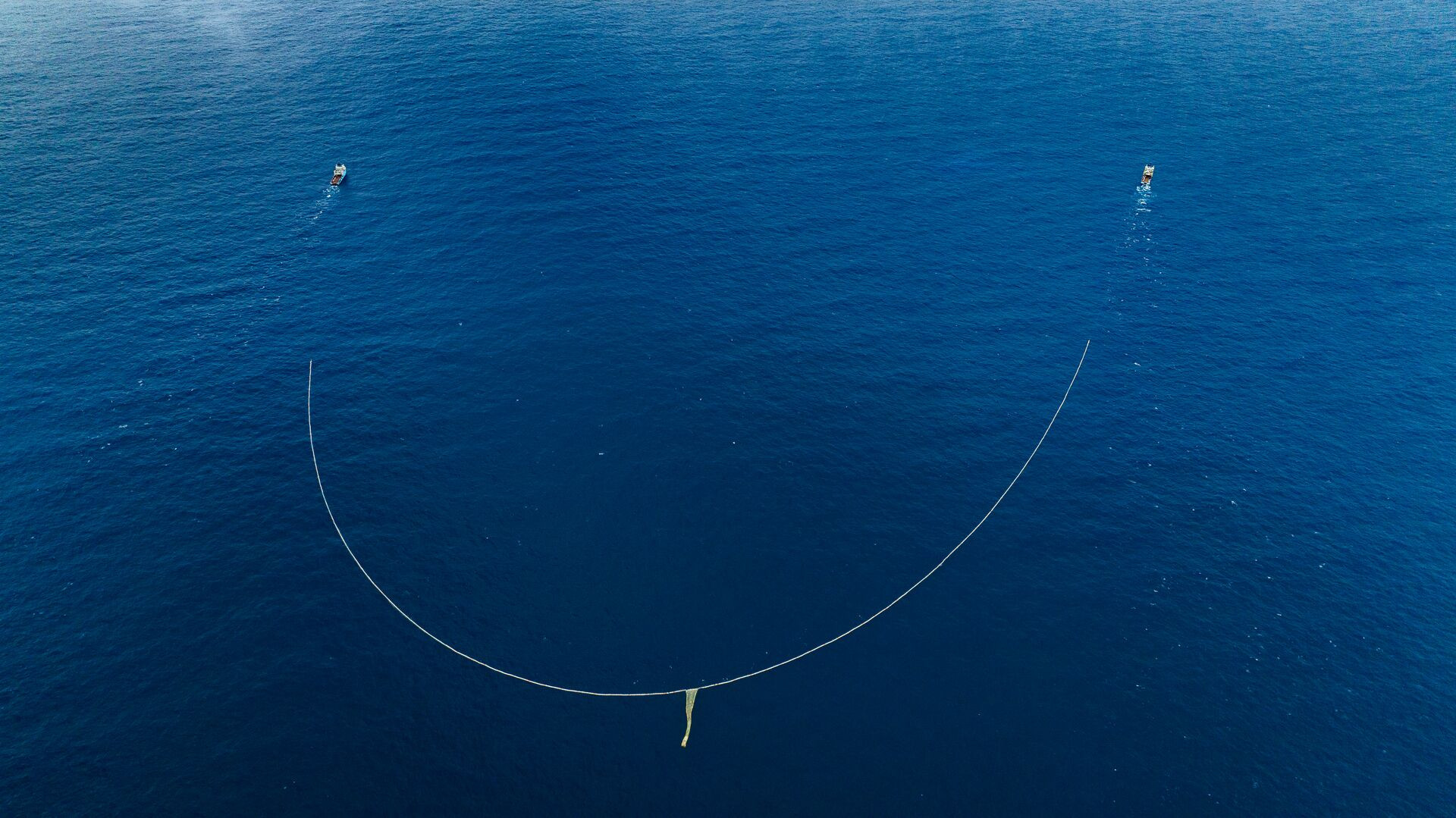 Na foto aérea, os dois barcos (canto superior da imagem) arrastam uma rede pelo Oceano, em projeto de coleta de plásticos da organização The Ocean Cleanup (Foto: The Ocean Cleanup)