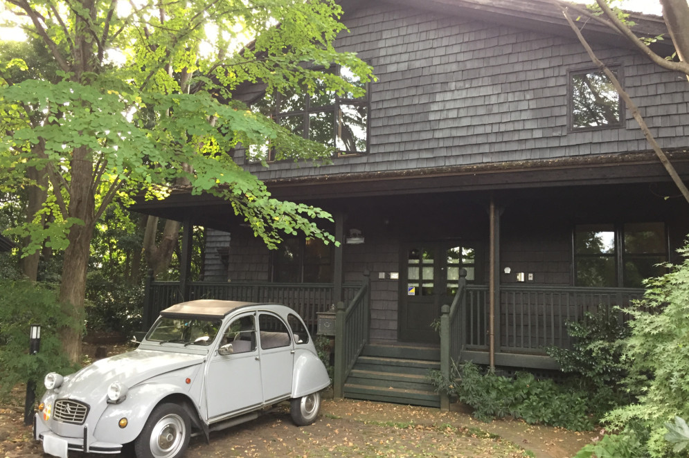 O estúdio pessoal de Miyazaki, chamado de Nibaraki, criado em 1984. A casa tem um estilo rústico, com paredes de madeira escura e janelas grandes, rodeado de árvores. Na frente, há uma pequena escada que leva à porta da entrada. Um carro antigo, de cor cinza claro e com teto de lona, está estacionado perto da casa(Foto: Wikicommons)