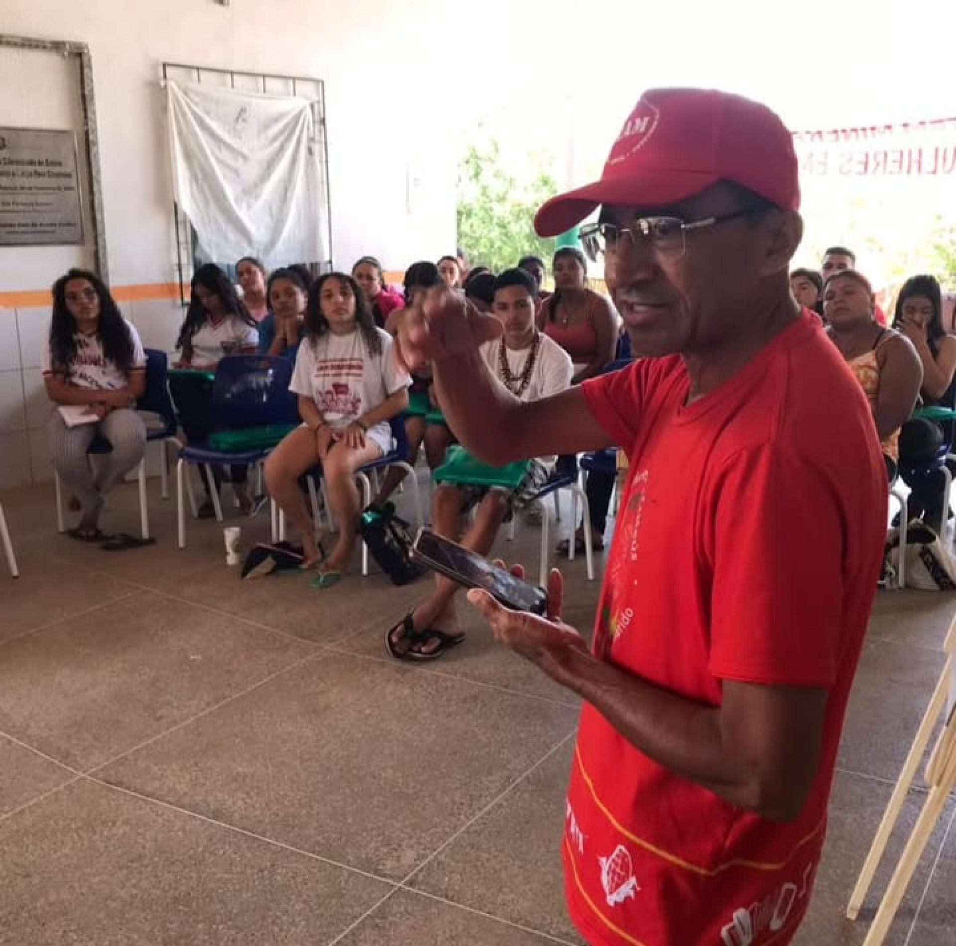 Para todos verem: imagem mostra José Ribamar do Nascimento, pescador de Novo Oriente. Ele está em primeiro plano, de perfil, de boné e camiseta vermelhos. Fala para um público