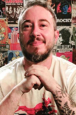 ParaTodosVerem: Tiago Cavalcante é um homem branco, de barba e cabelo curto grisalho. Ele está sorrindo, com as mãos cruzadas à frente do rosto(Foto: Reprodução/ Arquivo pessoal)