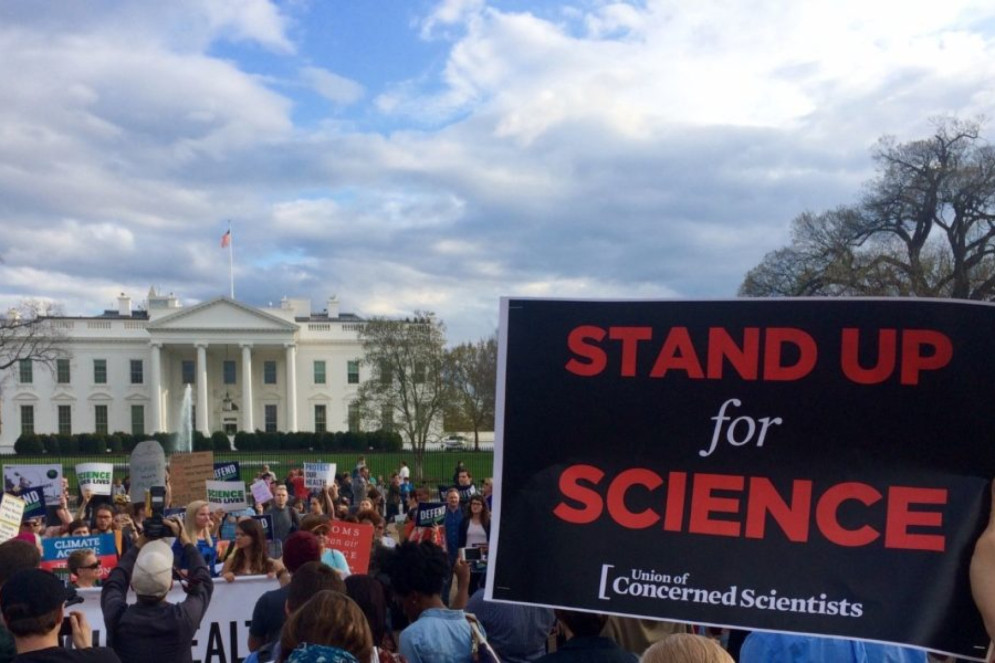 ParaTodosVerem: A foto mostra um protesto feito pela Union of Concerned Scientists em frente à Casa Branca, em Washignton, nos Estados Unidos. Em primeiro plano, vê-se um cartaz com a frase "levante-se pela ciência", escrito em inglês, e ao fundo, dezenas de pessoas aglomeradas na manifestaçaõ(Foto: Union of Concerned Scientists )