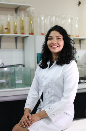 A imagem mostra Nicole Evelyn sentada em uma bancada do laboratório onde ela faz aulas práticas do curso de Ciências Biológicas da Uece(Foto: FÁBIO LIMA)
