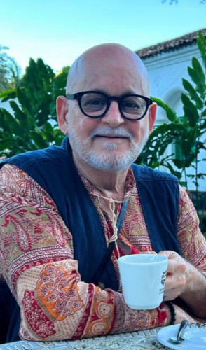 ParaTodosVerem: João Saraiva, fundador do movimento SOS Cocó. É um homem branco, de barba branca, sem cabelos. Usa óculos pretos e segura um copo branco. Usa uma camisa vermelha com um colete azul(Foto: Arquivo Pessoal/João Saraiva)