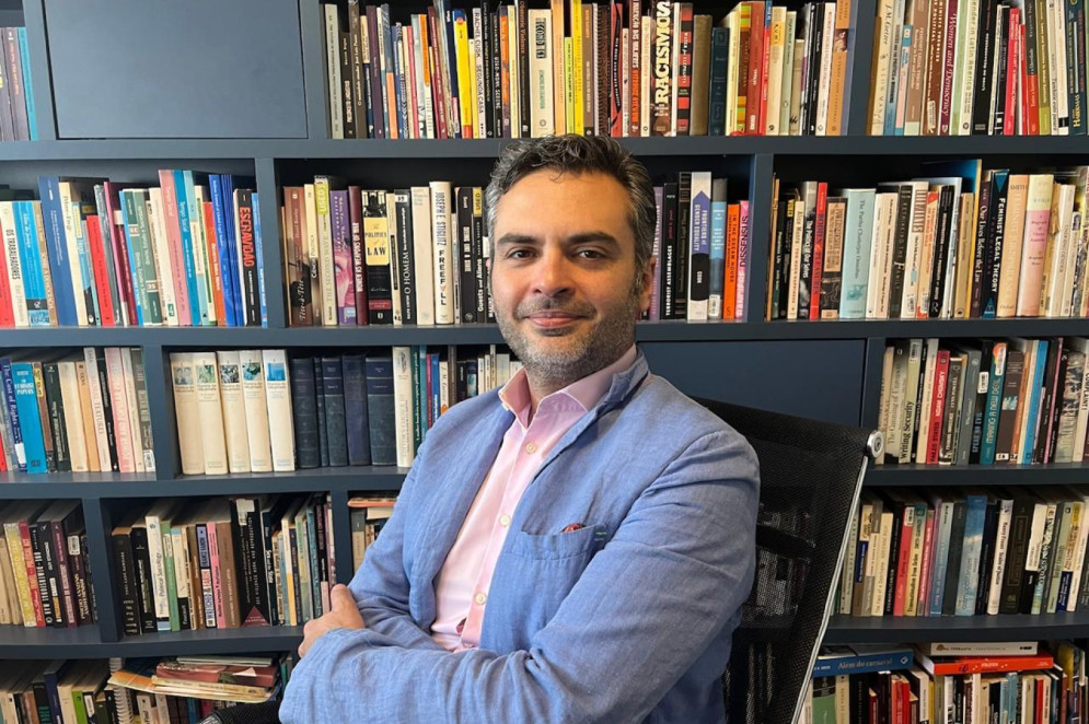 ParaTodosVerem: Pablo Holmes, professor associado no Instituto de Ciência Política da Universidade de Brasília (UnB). É um homem branco de cabelos com fios brancos. Está em frente a uma parede de livros. Usa blazer azul com camisa rosa(Foto: Arquivo Pessoal/Pablo Holmes)