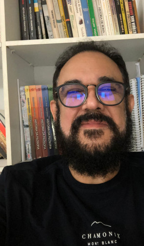 ParaTodosVerem: professor Sérgio Feitosa, de História, Sociologia e Filosofia. É um homem de cabelos e barba pretos, camisa preta. Está de frente a uma estante de livros(Foto: Arquivo Pessoal/Sérgio Feitosa)