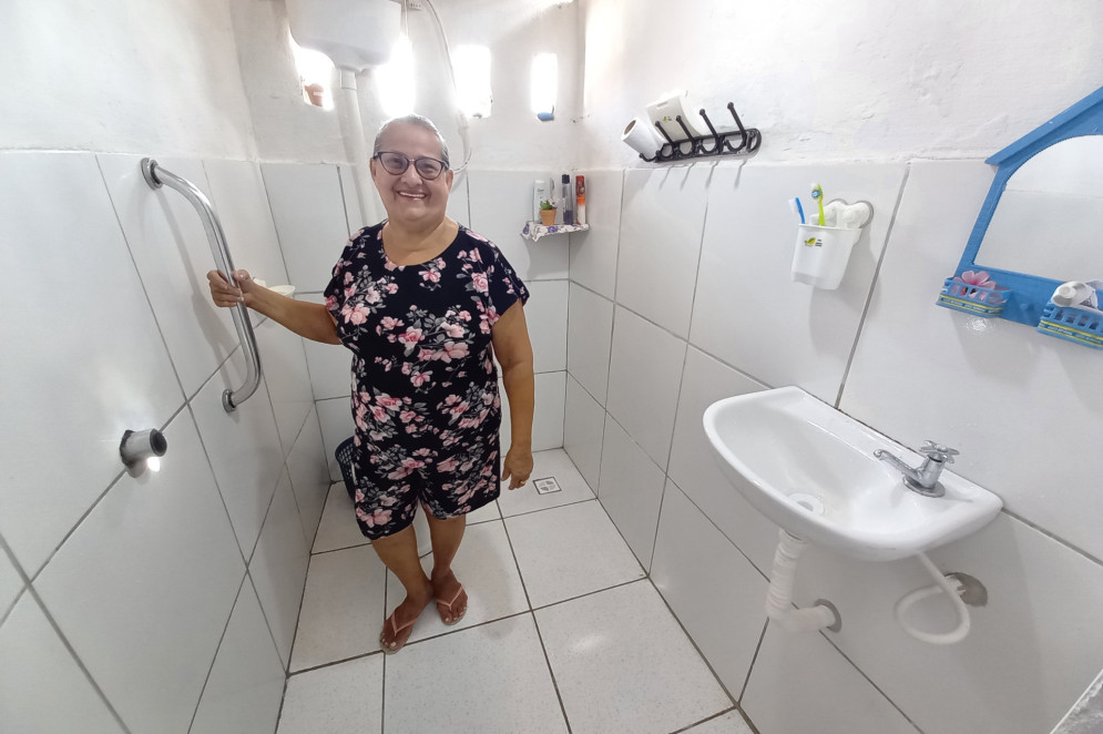 Dona Fátima, outra beneficiária do programa Morar Bem, da Habitafor, mostra seu novo banheiro após a reforma feita pelo projeto na casa dela(Foto: Divulgação/Habitafor)