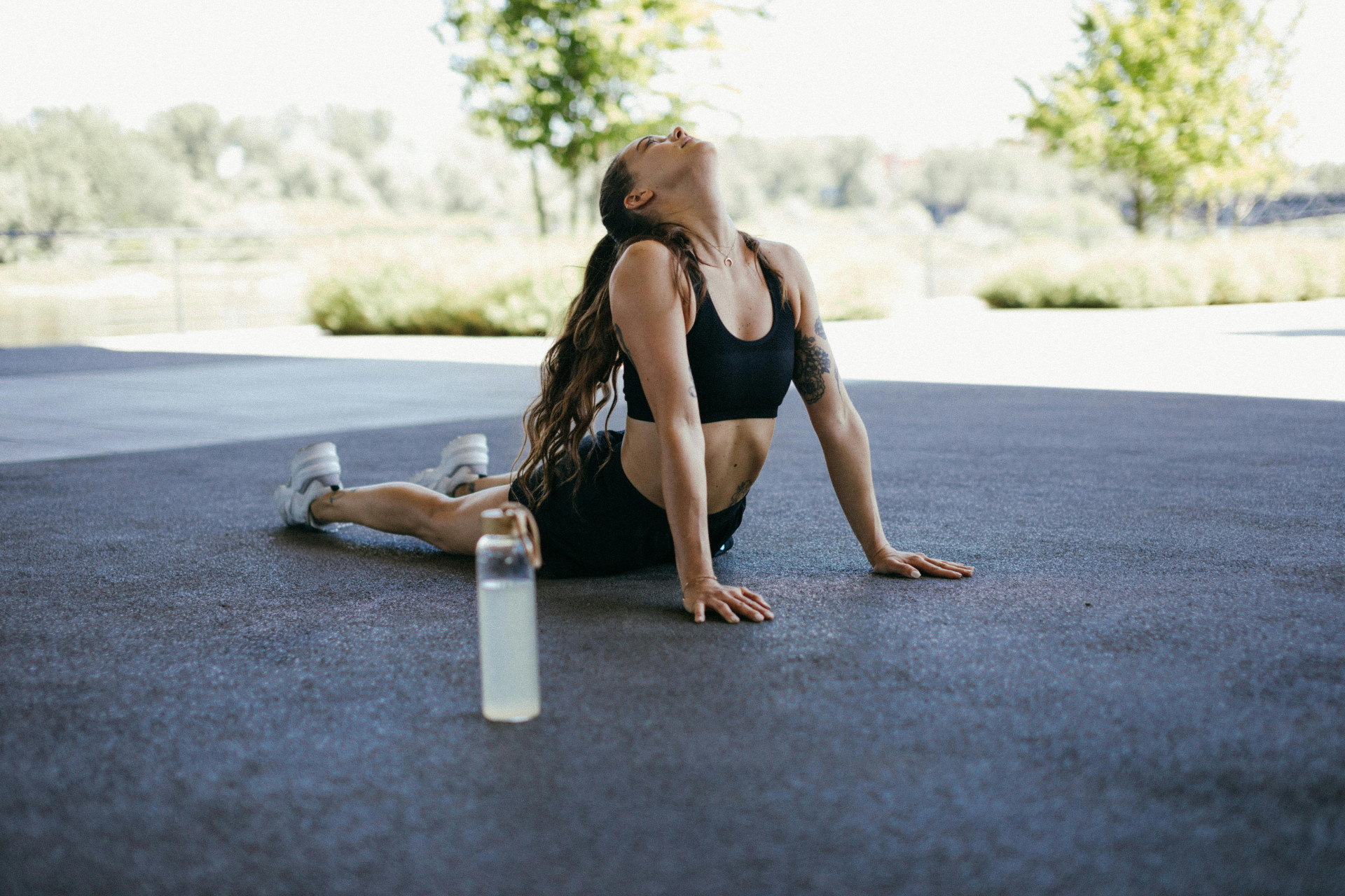 ParaTodosVerem: uma mulher está fazendo alongamento em uma área externa, com roupas esportivas pretas. Ela apoia as mãos no chão e estica o corpo para trás, olhando para cima (Foto: Pexels/KoolShooters)