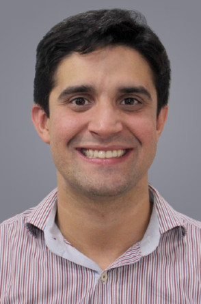 ParaTodosVerem: Gustavo Cabral é um homem branco, de cabelos escuros e camisa listrada. Sorridente, ele olha diretamente para a câmera contra um fundo cinza liso(Foto: Acervo pessoal / Lattes)