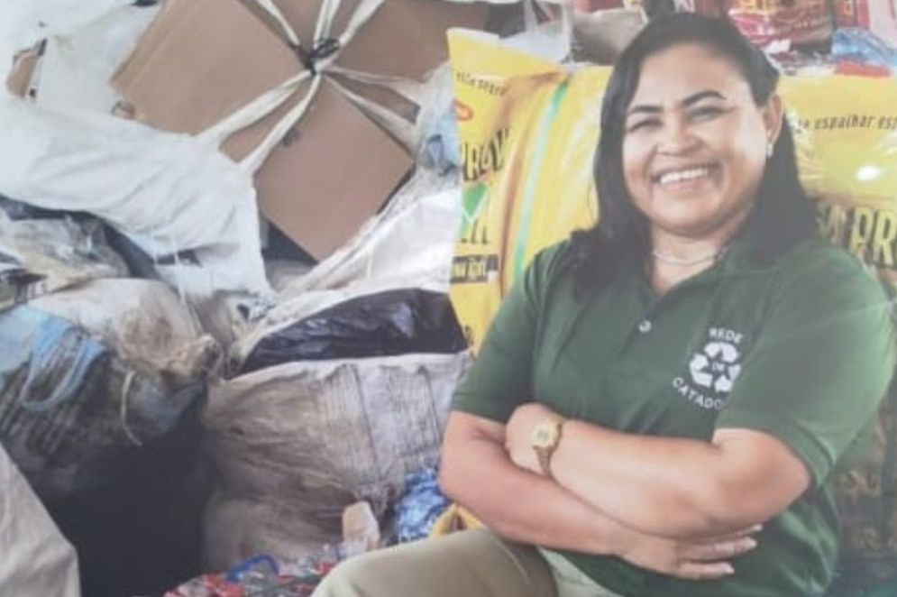Leina Mara é uma mulher negra de cabelo liso, curto e preto. Na imagem, ela está de braços cruzados ao lado de materiais recicláveis coletados(Foto: Reprodução/ Acervo pessoal)