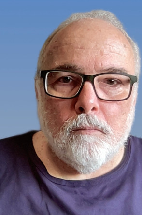 M&aacute;rio Azevedo &eacute; um  homem branco de cabelos e barba grisalhos. Ele usa &oacute;culos e na imagem veste uma blusa azul em um fundo azul(Foto: Reprodu&ccedil;&atilde;o/ Acervo pessoal)