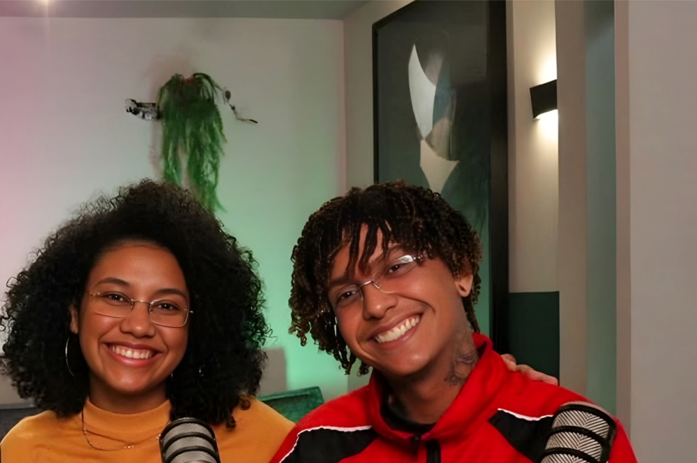 ParaTodosVerem: Na imagem, Carl e Nair, idealizadores da Mancuda. Nair, à esquerda, é uma mulher negra de cabelos cacheados, usa óculos de grau e uma camiseta amarela. Carll, à direita, é um homem negro, de cabelos também cacheados, usa óculos e, veste uma jaqueta esportiva vermelha e preta(Foto: Arquivo Pessoal)