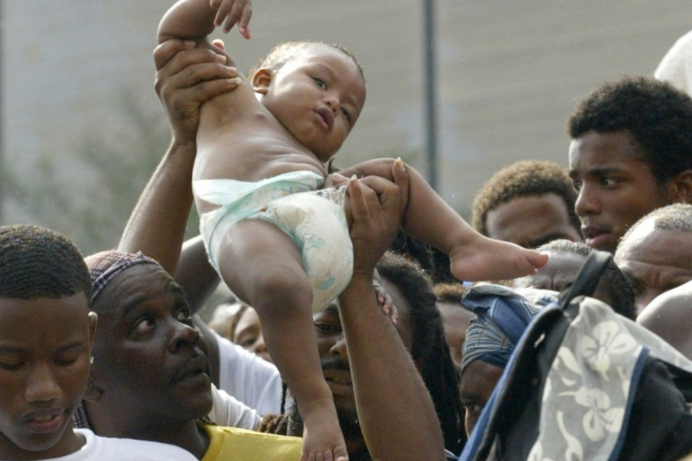 ParaTodosVerem: Um bebê é passado por cima da multidão enquanto as pessoas esperam para sair do ginásio Superdome, em Nova Orleans, em  2005(Foto: James Nielsen / AFP)