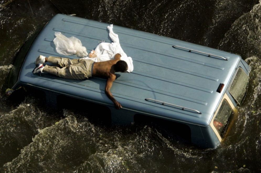 ParaTodosVerem: Um homem se agarra ao teto de um veículo antes de ser resgatado pela Guarda Costeira dos EUA das ruas inundadas após o furacão Katrina em Nova Orleans, em 4 de setembro de 2005(Foto: Robert Galbraith / AFP)